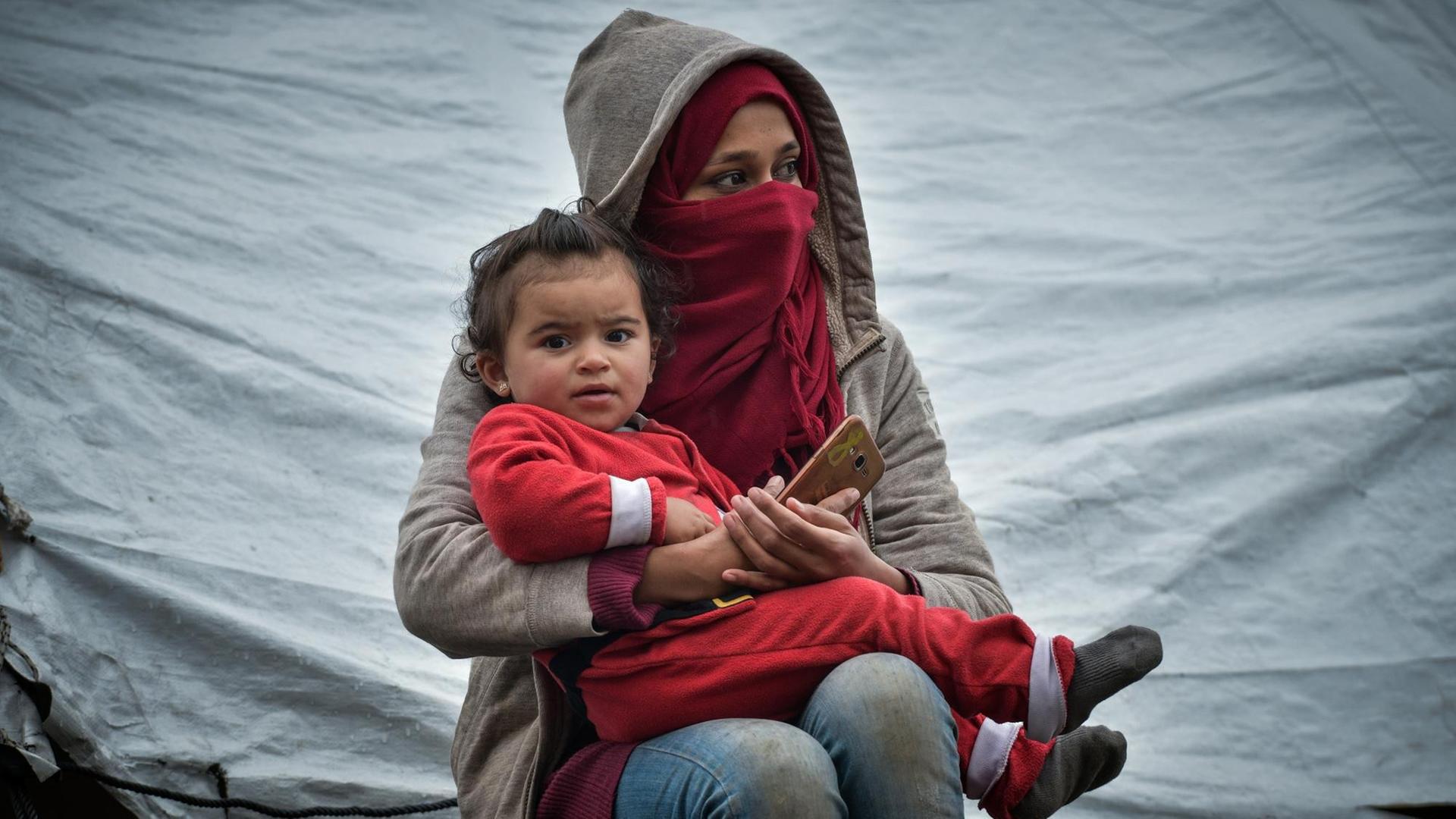 Momentaufnahme aus dem Flüchtlingslager Moria auf der Insel Lesbos am 10.03.2020. Zu sehen ist eine junge Frau, die ein kleines Kind im Arm hält. Momentaufnahme aus dem Flüchtlingslager Moria auf der Insel Lesbos am 10.03.2020. Zu sehen ist eine junge Frau, die ein kleines Kind im Arm hält.