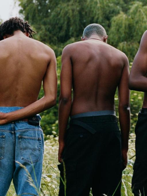Fünf schwarze Jungs stehen oberkörperfrei in einer Wiese.