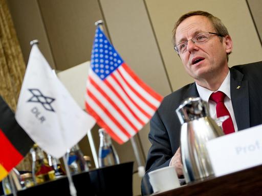 Johann-Dietrich Wörner bei einer Pressekonferenz hinter Flaggen Deutschlands, der USA und des Deutschen Zentrums für Luft- und Raumfahrt.