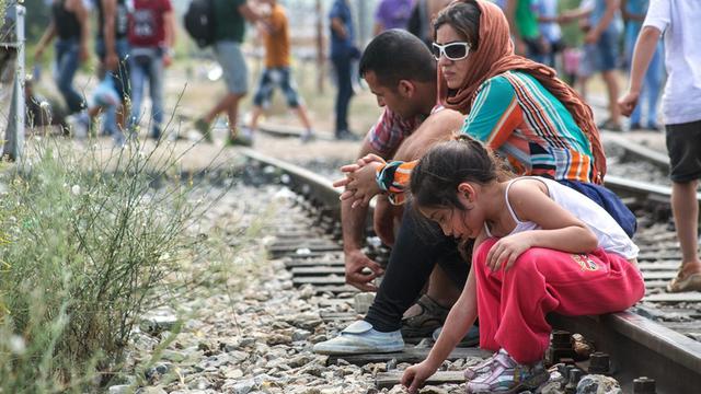 Eine Familie sitzt an der griechisch-mazedonischen Grenze auf Gleisen und wartet.