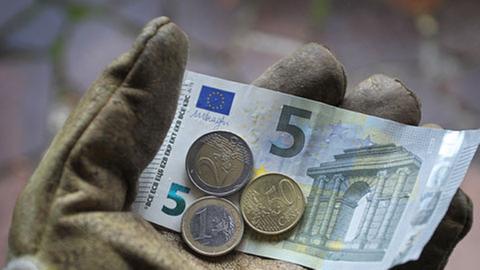 Eine Hand in einem Arbeitshandschuh hält acht Euro und fünfzig Cent.
