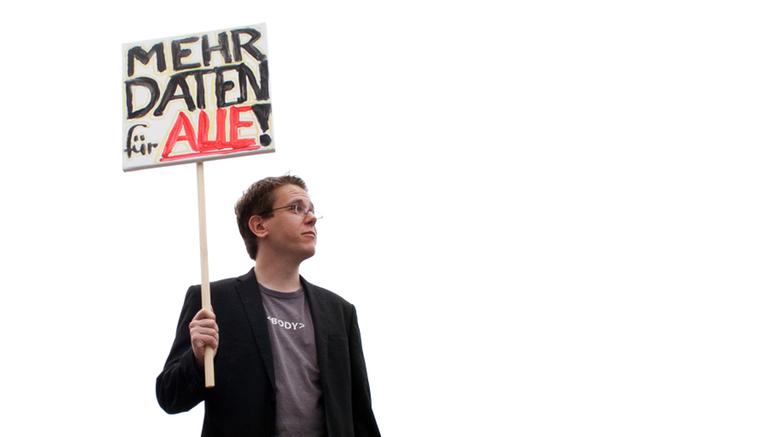 Datenjournalist Michael Kreil hält ein Schild in der Hand, auf dem steht "Mehr Daten für alle".