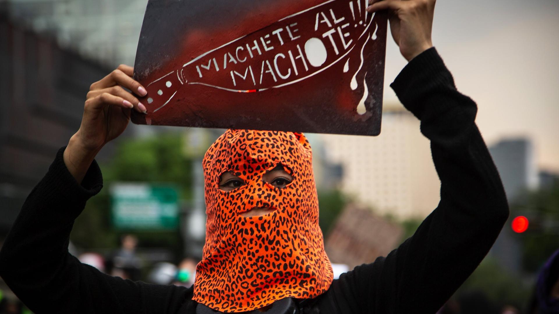 Eine Demonstrantin, in einer Leopardenmuster-Maske, bei Protesten gegen Femizide in Mexiko Stadt, mit einem Schild mit der Aufschrift "Machete all Machote!!!" Eine Demonstrantin, in einer Leopardenmuster-Maske, bei Protesten gegen Femizide in Mexiko Stadt, mit einem Schild mit der Aufschrift "Machete all Machote!!!"