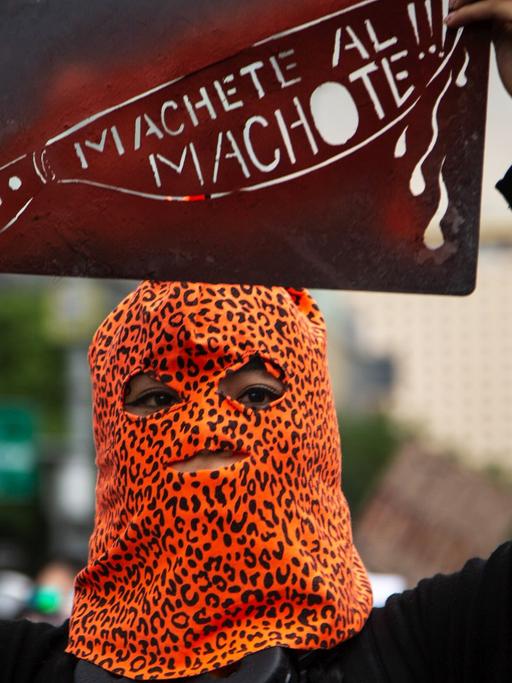 Eine Demonstrantin, in einer Leopardenmuster-Maske, bei Protesten gegen Femizide in Mexiko Stadt, mit einem Schild mit der Aufschrift "Machete all Machote!!!"