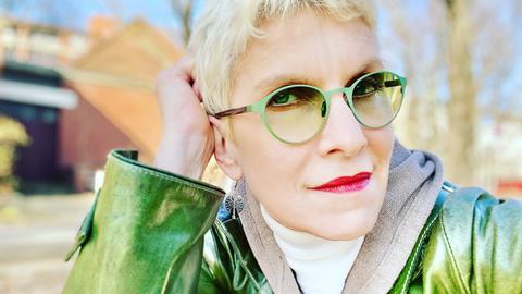 Portrait der Schriftsteller*in Else Buschheuer in grünem Mantel und mit grüner Sonnenbrille.