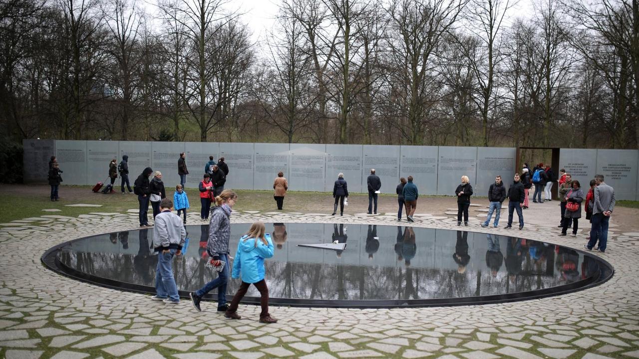 Menschen stehen in Berlin um das Denkmal für die im Nationalsozialismus ermordeten Sinti und Roma.