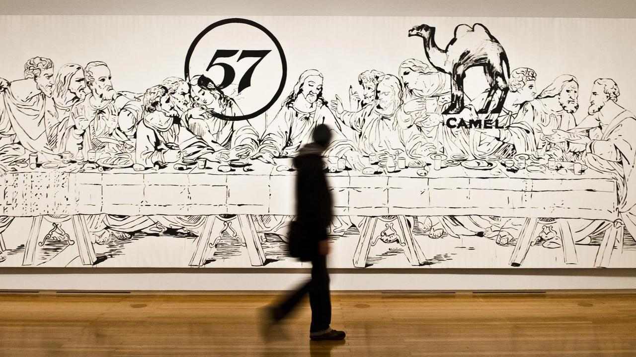 Eine Besucherin schreitet entlang des Bildes "The Last Supper (Camel/57)" in einem Ausstellungsraum der Frankfurter Schirn, welches das Motiv des Abendmahls in Kombination mit Bezügen der Konsumgesellschaft verbindet.