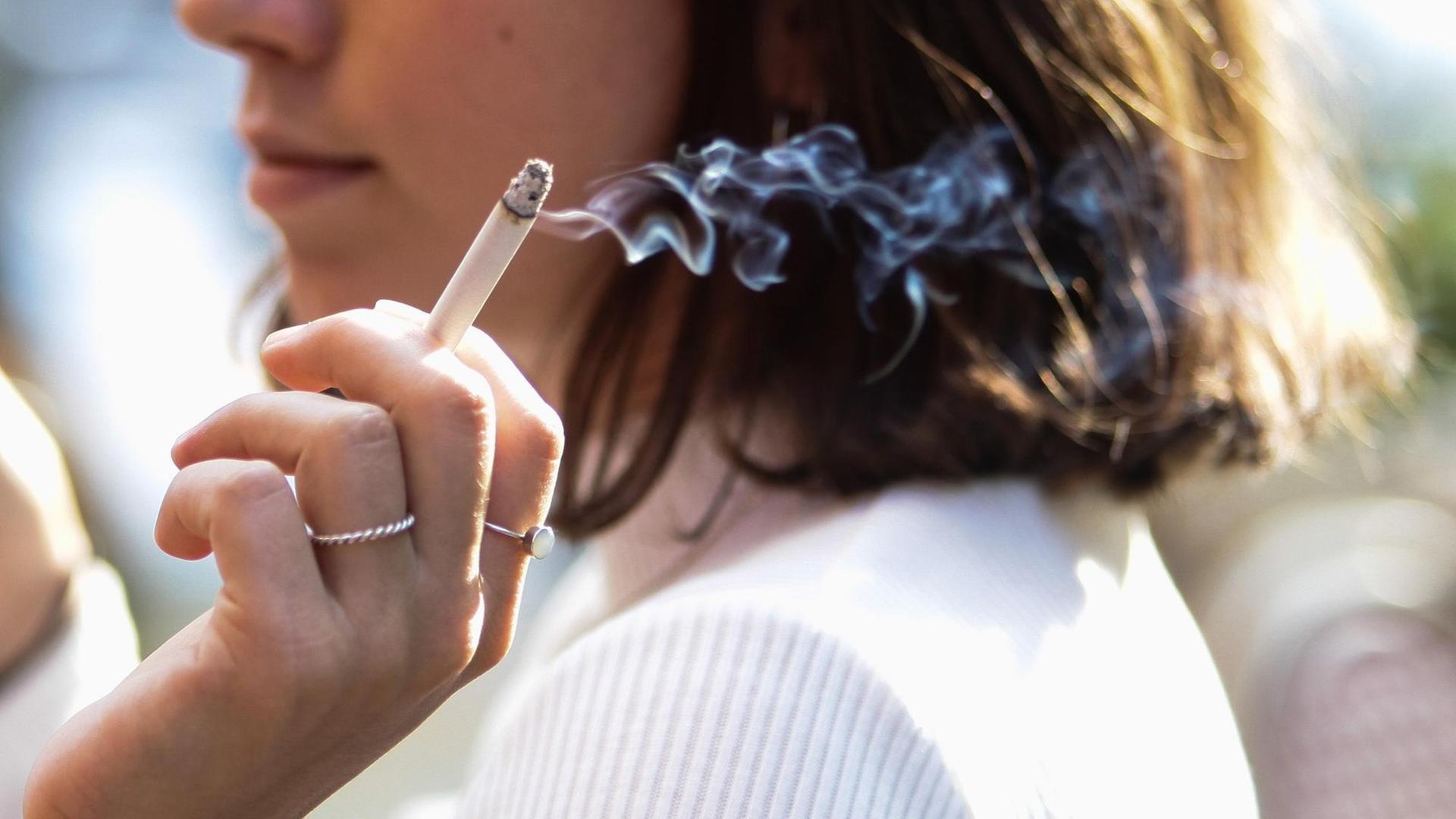 Eine junge Frau sitzt auf der Terrasse eines Cafes und raucht eine Zigarette. Eine junge Frau sitzt auf der Terrasse eines Cafes und raucht eine Zigarette.