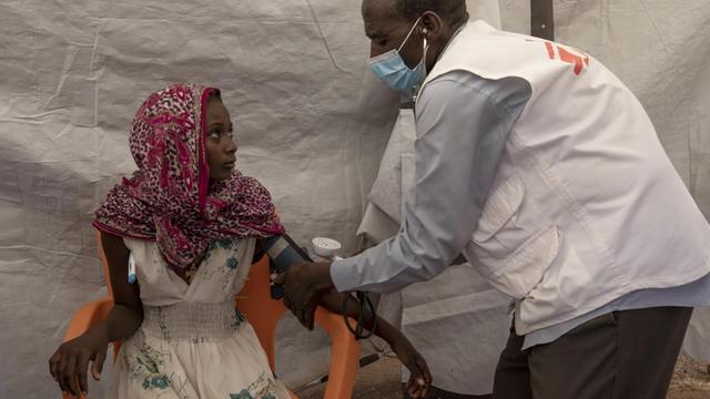 Ein Krankenpfleger von Ärzte ohne Grenzen misst Blutdruck und Fieber bei einer jungen Frau aus Tigray, die vor dem Konflikt in ihrer Region geflohen ist, in dem Camp für Geflüchtete Umm Rakouba, in Qadarif im Osten Sudans, aufgenommen am 5. Dezember 2020.