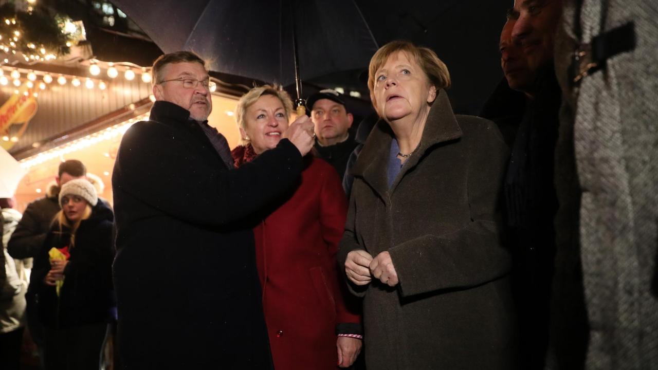 Knapp ein Jahr nach dem Terroranschlag besucht Bundeskanzlerin Angela Merkel (CDU, r) den Breitscheidplatz in Berlin und unterhält sich mit dem Betreiber eines Bratwurst-Standes.