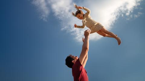 Ein Mädchen wird von seinem Vater in die Luft geworfen.