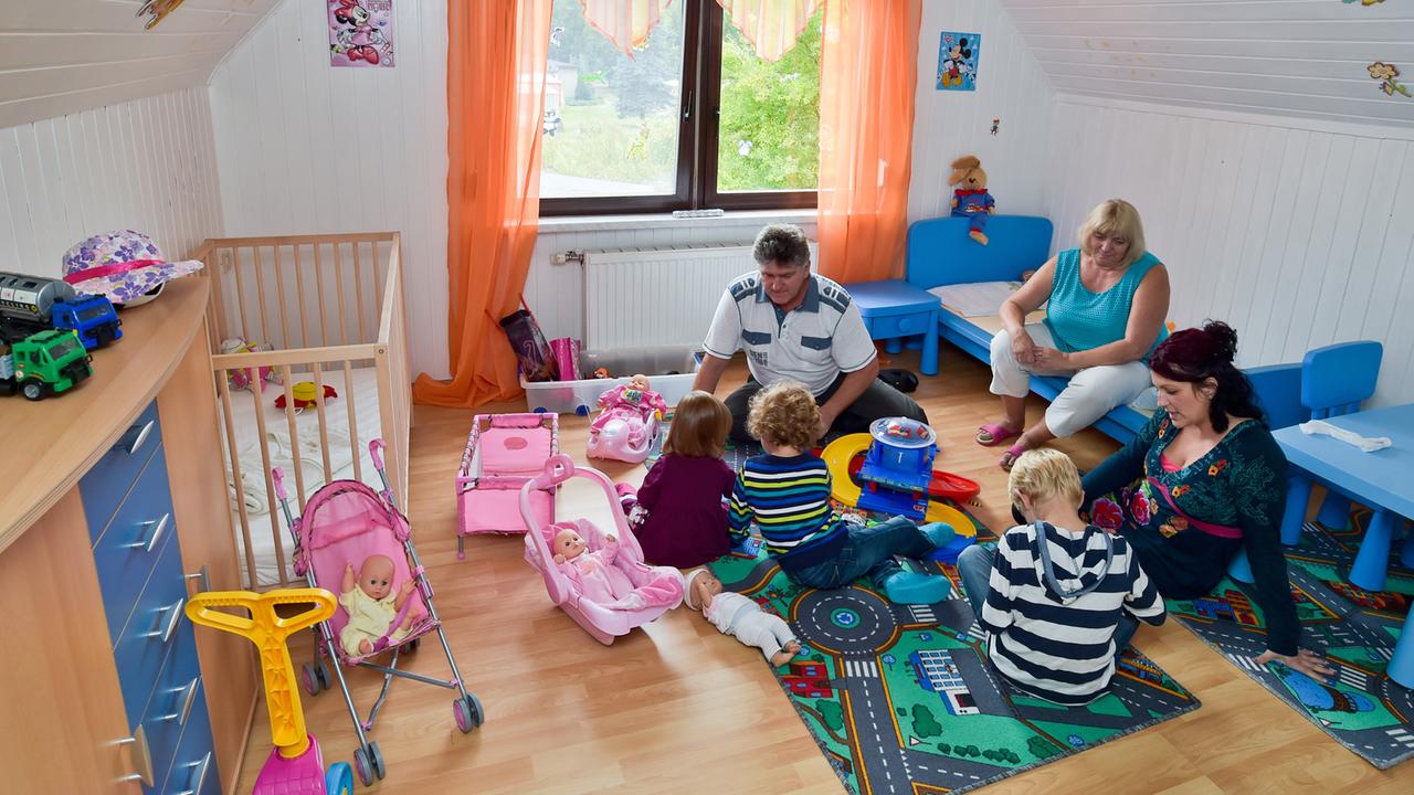 Pflegeeltern mit ihren drei Pflegekindern: Auf dem Boden sitzt eine Mitarbeiterin des Jugendamts und unterhält sich mit dem ältesten Jungen.
