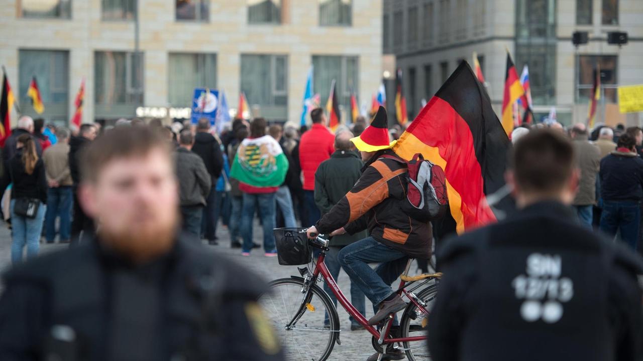 Ein Anhänger der islamfeindlichen Pegida-Bewegung fährt am 27.03.2017 mit einem Fahrrad und einer Deutschlandfahne während einer Kundgebung über den Altmarkt in Dresden (Sachsen). Die "Patriotischen Europäer gegen die Islamisierung des Abendlandes" (Pegida) hatten zu einer Kundgebung in Sachsens Landeshauptstadt aufgerufen. Gleichzeitig haben mit einem Überraschungsauftritt die Toten Hosen ein Zeichen gegen Rechts gesetzt. Foto: Arno Burgi/dpa-Zentralbild/dpa | Verwendung weltweit Ein Anhänger der islamfeindlichen Pegida-Bewegung fährt am 27.03.2017 mit einem Fahrrad und einer Deutschlandfahne während einer Kundgebung über den Altmarkt in Dresden (Sachsen). Die "Patriotischen Europäer gegen die Islamisierung des Abendlandes" (Pegida) hatten zu einer Kundgebung in Sachsens Landeshauptstadt aufgerufen. Gleichzeitig haben mit einem Überraschungsauftritt die Toten Hosen ein Zeichen gegen Rechts gesetzt. Foto: Arno Burgi/dpa-Zentralbild/dpa | Verwendung weltweit