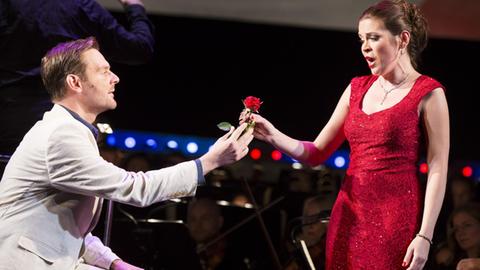Sänger Daniel Jenz und Sängerin Sieglinde Feldhofer auf der Bühne in einer Szene der Operette "Clo-Clo" von Franz Lehár. Jenz gibt Feldhofer eine rote Rose.