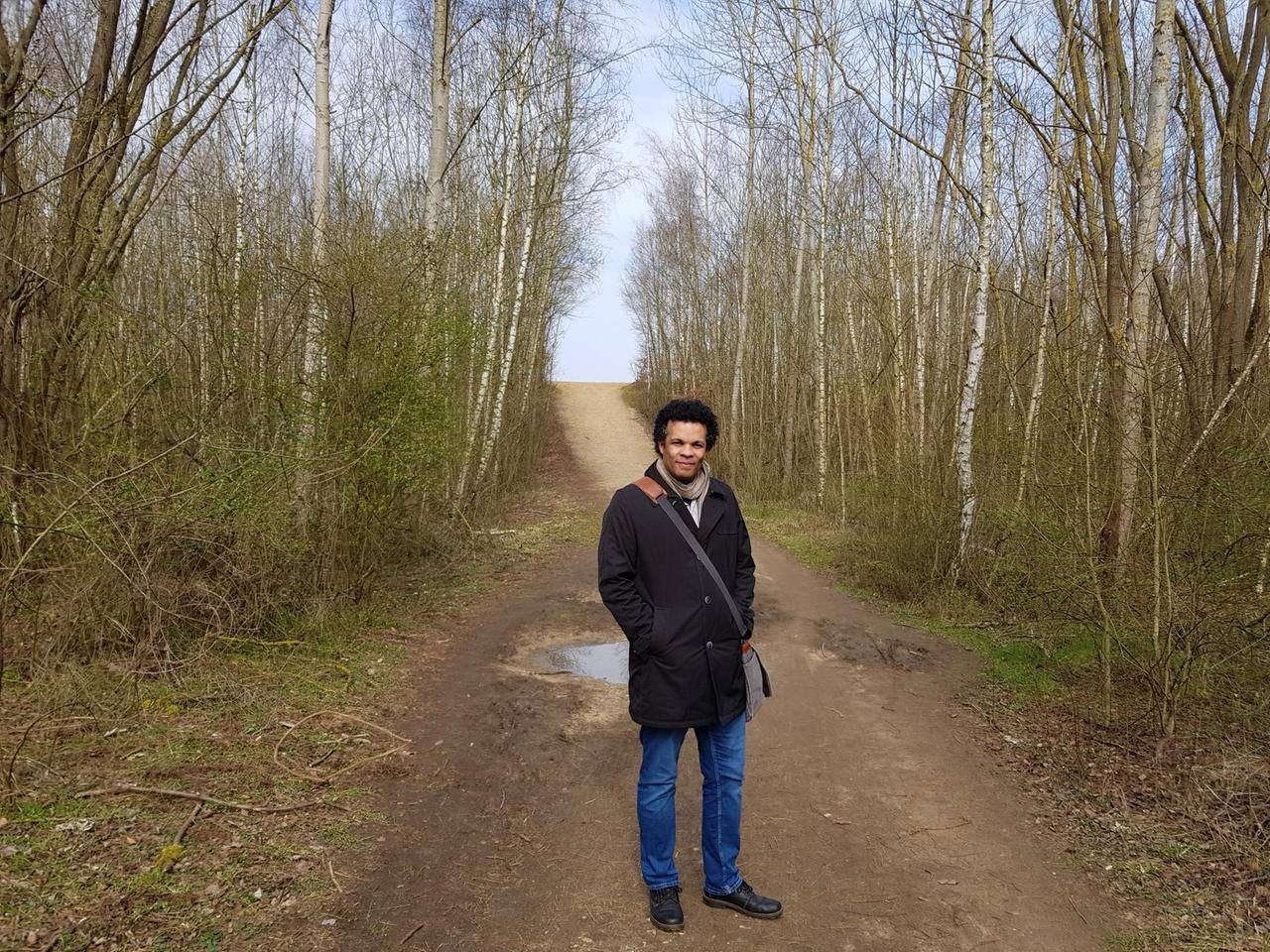 James A. Sullivan steht auf einem Weg umringt von Birken. Er schaut leicht lächelnd in die Kamera. Der Fluchtpunkt bildet sich in dem Zusammentreffen von Waldweg und Himmel. James A. Sullivan steht auf einem Weg umringt von Birken. Er schaut leicht lächelnd in die Kamera. Der Fluchtpunkt bildet sich in dem Zusammentreffen von Waldweg und Himmel.