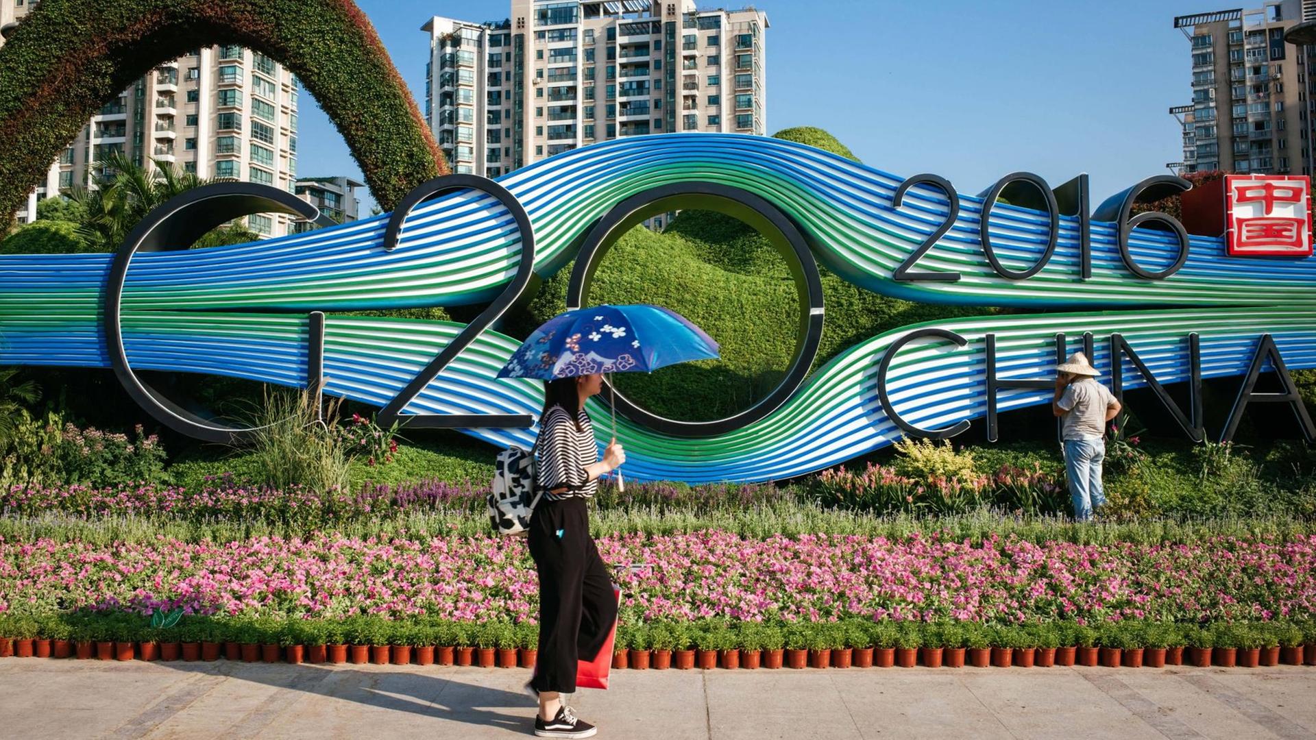 Chinesen laufen in Hangzhou an einem Blumenbeet mit dem G20-Logo vorbei.