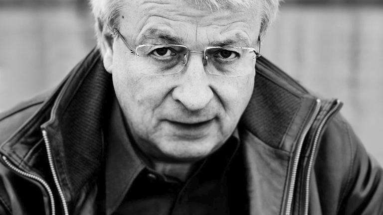 Schwarzweißaufnahme des Autors. Er trägt Brille und Lederjacke und schaut in die Kamera. Schwarzweißaufnahme des Autors. Er trägt Brille und Lederjacke und schaut in die Kamera.