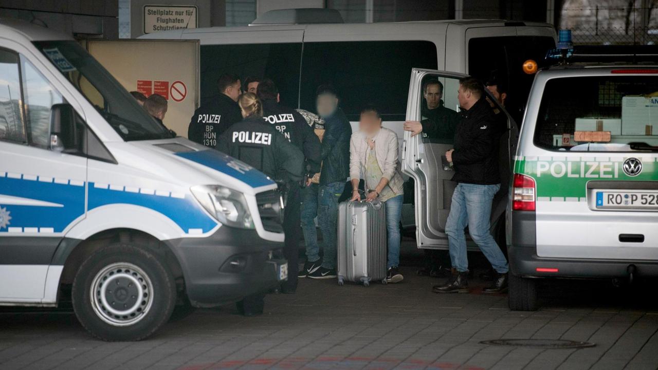 Mit Handschellen gefesselt schiebt ein Mann am Frankfurter Flughafen seinen Rollkoffer zwischen Polizisten hindurch, ein anderer trägt einen Pappkarton. Mit Handschellen gefesselt schiebt ein Mann am Frankfurter Flughafen seinen Rollkoffer zwischen Polizisten hindurch, ein anderer trägt einen Pappkarton.