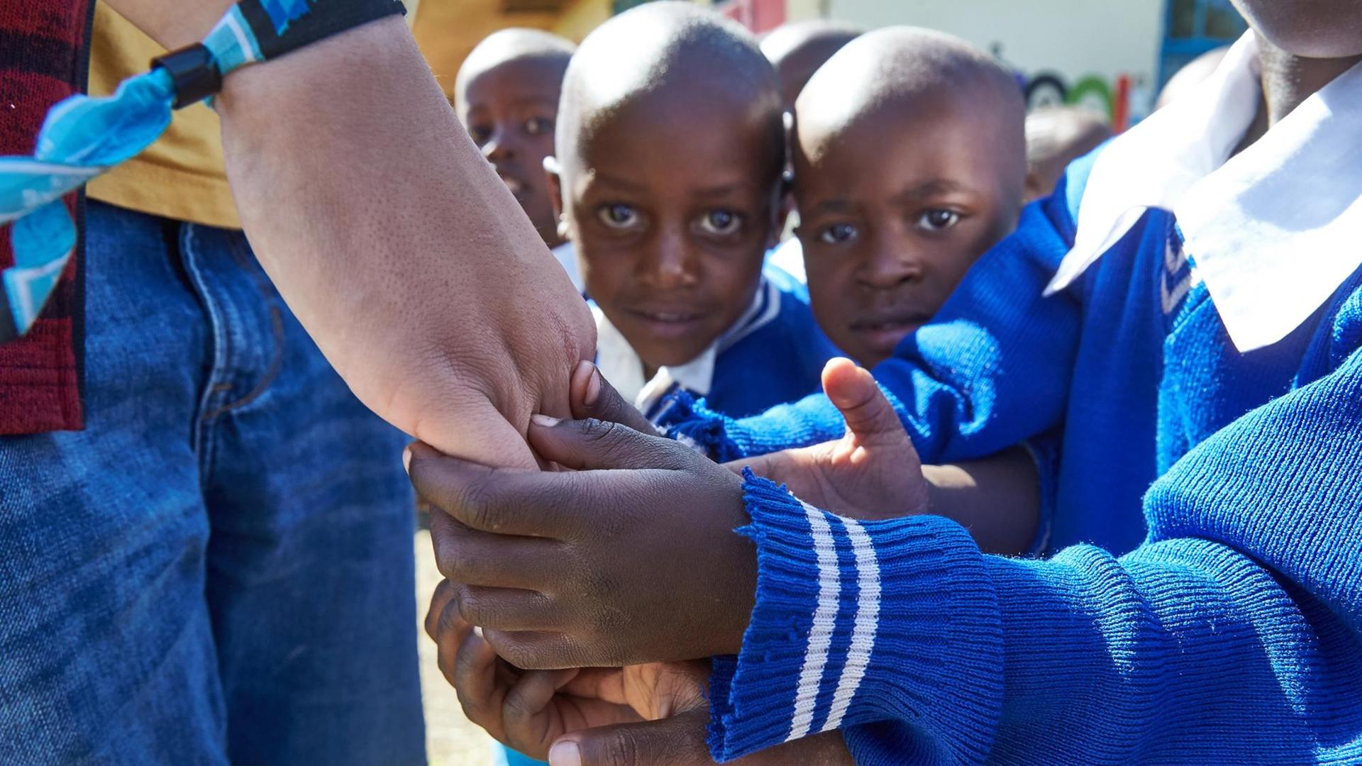 Zwei kleine afrikanische Jungen halten die Hand eines Weißen fest.