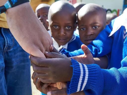 Zwei kleine afrikanische Jungen halten die Hand eines Weißen fest.