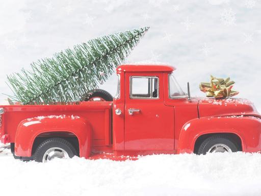 Ein Modell-Pickup-Truck im Schnee mit Weihnachtsbaum auf der Ladefläche