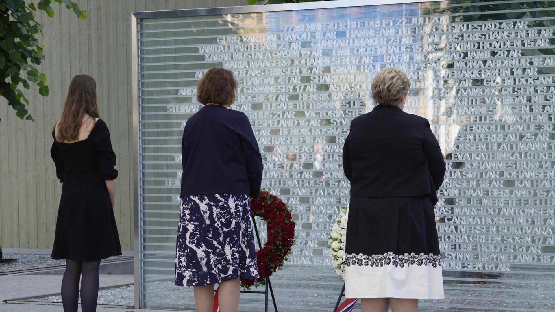 Erinnerung an das Massaker von Utoya 2011, drei Personen stehen vor einer Gedenktafel Erinnerung an das Massaker von Utoya 2011, drei Personen stehen vor einer Gedenktafel
