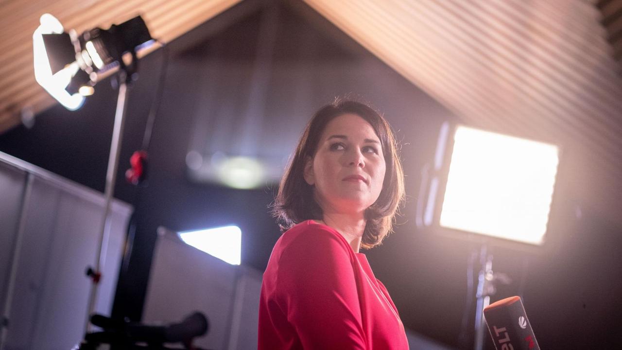 Annalena Baerbock, Bundesvorsitzende von Bündnis 90/Die Grünen, blickt am Rande eines Fernsehinterviews beim digitalen Bundesparteitag der Grünen in die Veranstaltungshalle. Scheinwerfer strahlen sie an. Annalena Baerbock, Bundesvorsitzende von Bündnis 90/Die Grünen, blickt am Rande eines Fernsehinterviews beim digitalen Bundesparteitag der Grünen in die Veranstaltungshalle. Scheinwerfer strahlen sie an.