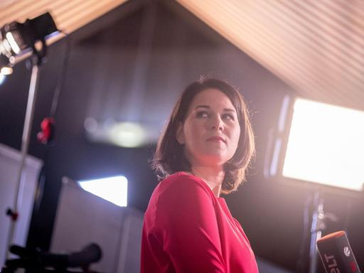 Annalena Baerbock, Bundesvorsitzende von Bündnis 90/Die Grünen, blickt am Rande eines Fernsehinterviews beim digitalen Bundesparteitag der Grünen in die Veranstaltungshalle. Scheinwerfer strahlen sie an.