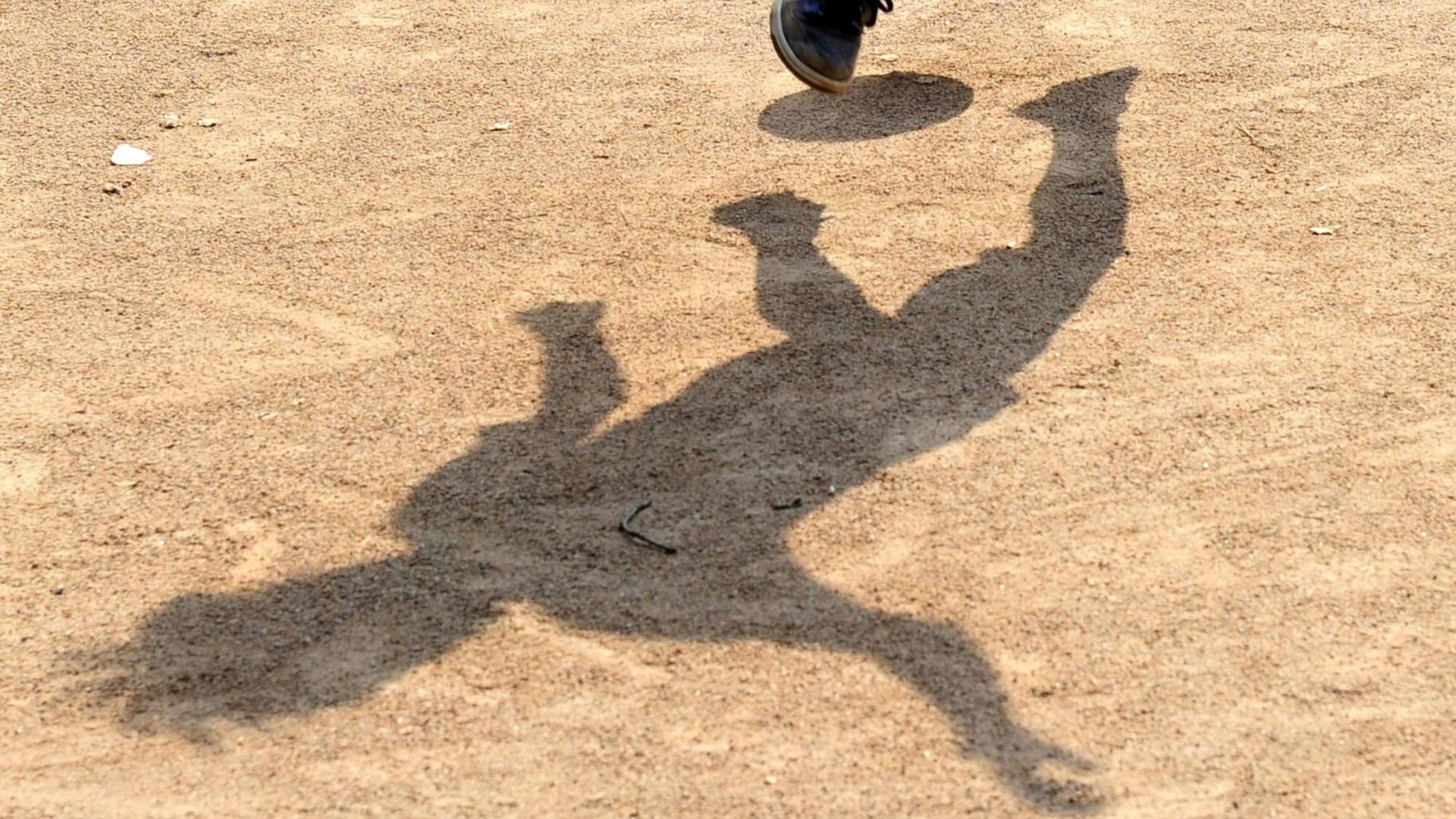 Der Schatten eines Jugendlichen mit einem Fußball zeichnet sich auf einem Bolzplatz ab Der Schatten eines Jugendlichen mit einem Fußball zeichnet sich auf einem Bolzplatz ab