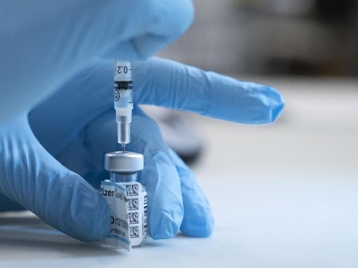 Der Corona-Impfstoff von Biontech und Pfizer. Eine Krankenschwester im UC Davis Medical Center in Sacramento, Kalifornien, zieht die Subsatnz aus einem Gläschen in eine Spritze. Zu sehen ist nur ihre mit einem blauen Handschuh geschützte Hand.