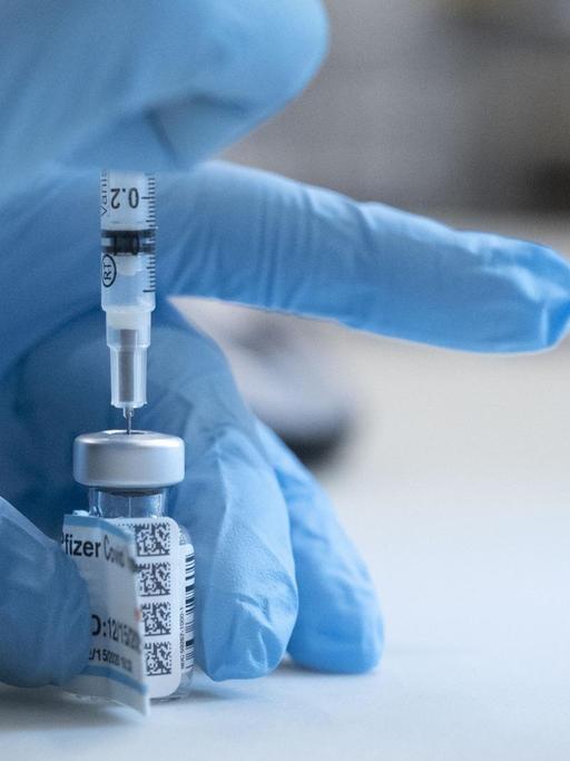 Der Corona-Impfstoff von Biontech und Pfizer. Eine Krankenschwester im UC Davis Medical Center in Sacramento, Kalifornien, zieht die Subsatnz aus einem Gläschen in eine Spritze. Zu sehen ist nur ihre mit einem blauen Handschuh geschützte Hand.