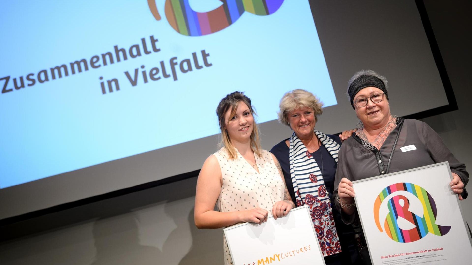 29.05.2018, Berlin: Monika Grütters (M,CDU), Kulturstaatsministerin zeichnet die drei besten Vorschläge der Aktion "Gib mir ein Zeichen" aus. Jennifer Leidorf (l) und Dorothee Herrmann gehörten zu den Preisträgern (Dritte Preisträgerin war nicht anwesend). Die Initiative Kulturelle Integration hatte dazu aufgerufen ein Zeichen zu entwerfen, das für Zusammenhalt in Vielfalt steht. Es wurden mehr als 780 Zeichen von Bürgerinnen und Bürgern vorgeschlagen. Foto: Sina Schuldt/dpa | Verwendung weltweit 29.05.2018, Berlin: Monika Grütters (M,CDU), Kulturstaatsministerin zeichnet die drei besten Vorschläge der Aktion "Gib mir ein Zeichen" aus. Jennifer Leidorf (l) und Dorothee Herrmann gehörten zu den Preisträgern (Dritte Preisträgerin war nicht anwesend). Die Initiative Kulturelle Integration hatte dazu aufgerufen ein Zeichen zu entwerfen, das für Zusammenhalt in Vielfalt steht. Es wurden mehr als 780 Zeichen von Bürgerinnen und Bürgern vorgeschlagen. Foto: Sina Schuldt/dpa | Verwendung weltweit