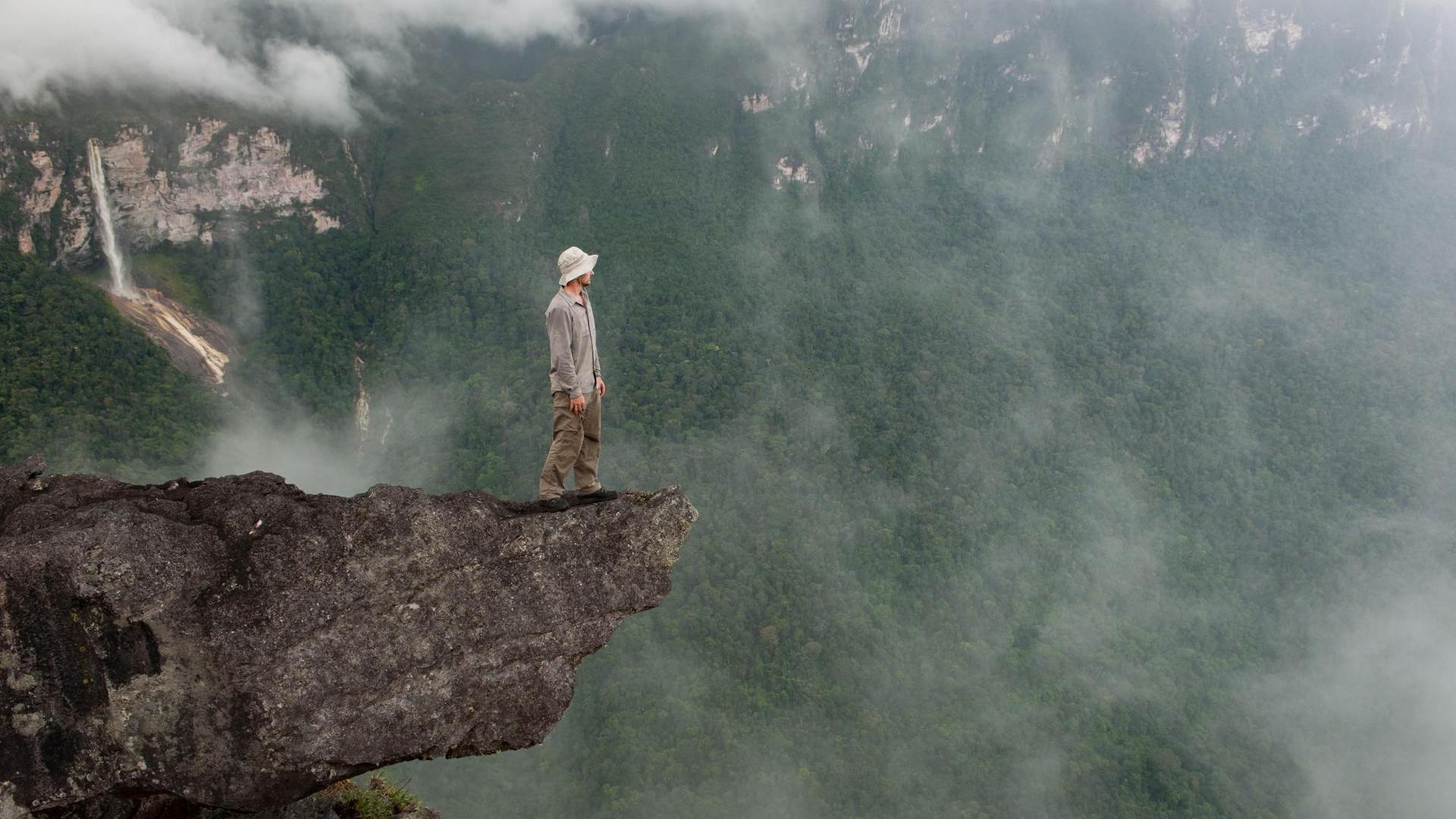 Markus Mauthe steht auf einem Felsvorsprung, im Hintergrund Regenwald