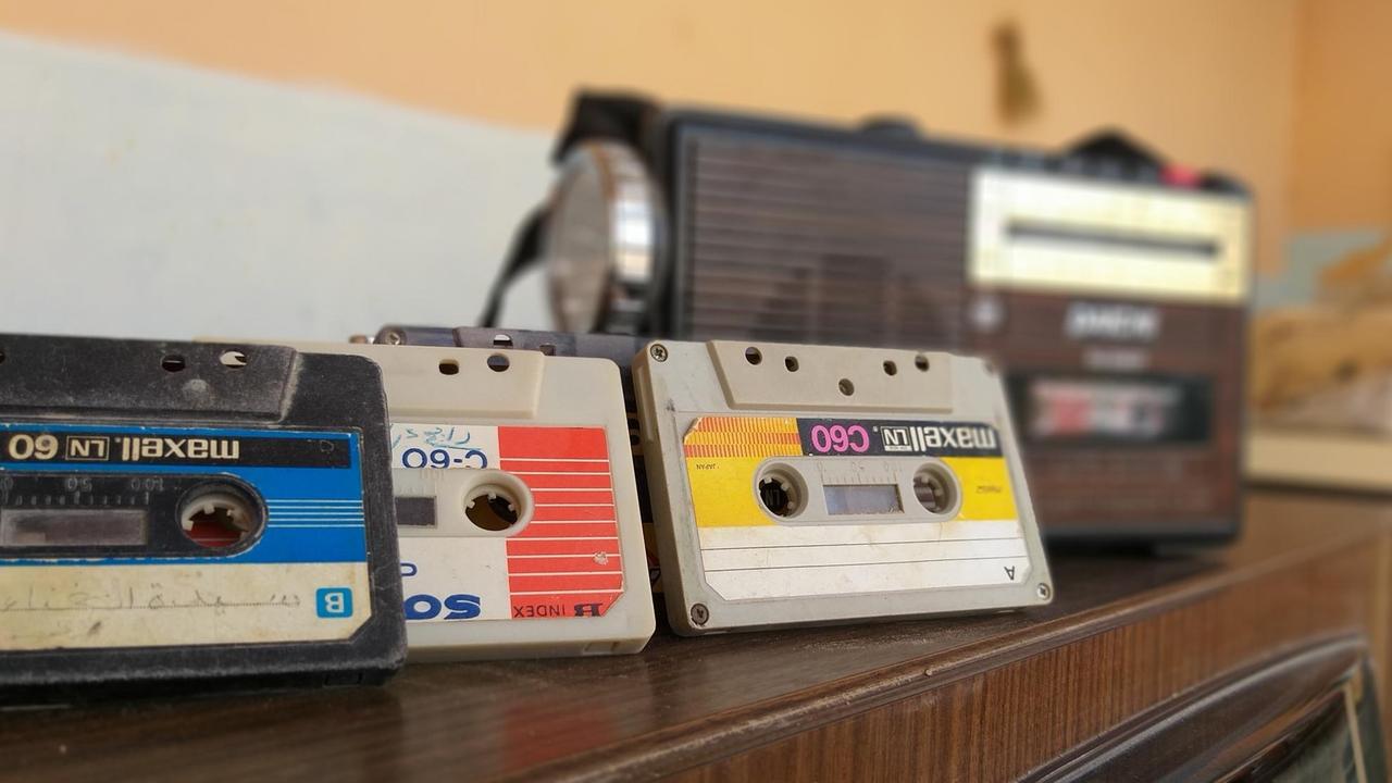 Drei Audiokassetten mit bunten Etiketten lehnen an einem alten Kassettenrecorder. Drei Audiokassetten mit bunten Etiketten lehnen an einem alten Kassettenrecorder.