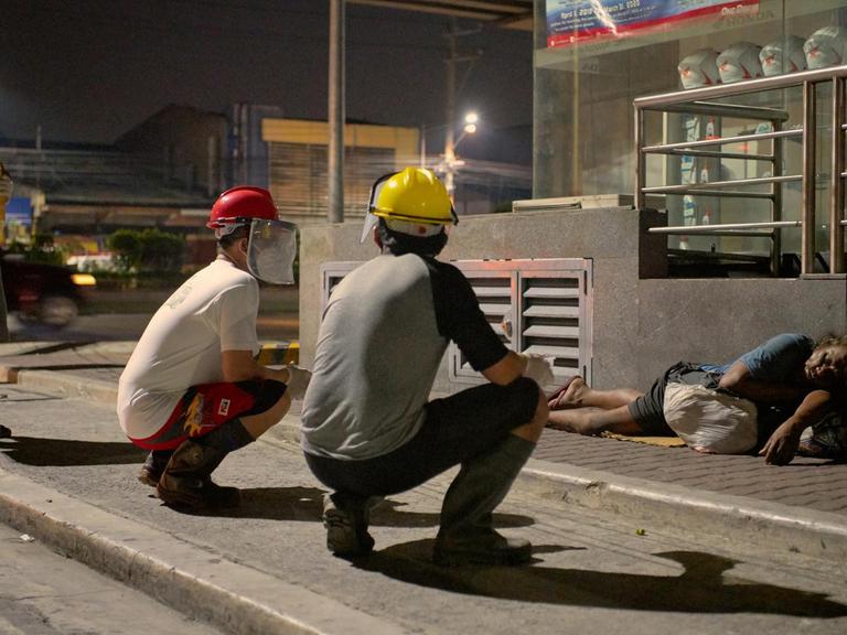 An Obdachlose werden auf einer Straße in Manila Essen und Maske verteilt.