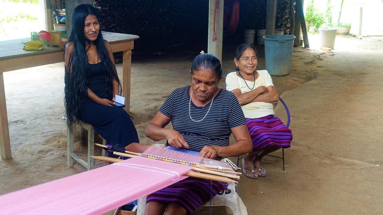 Links sitzt die 32-jährige Flora Reyes. Sie hat lange schwarze Haare. Vor ihr eine ältere Weberin bei der Arbeit. Dahinter lachend die ältere Doña China. Links sitzt die 32-jährige Flora Reyes. Sie hat lange schwarze Haare. Vor ihr eine ältere Weberin bei der Arbeit. Dahinter lachend die ältere Doña China.