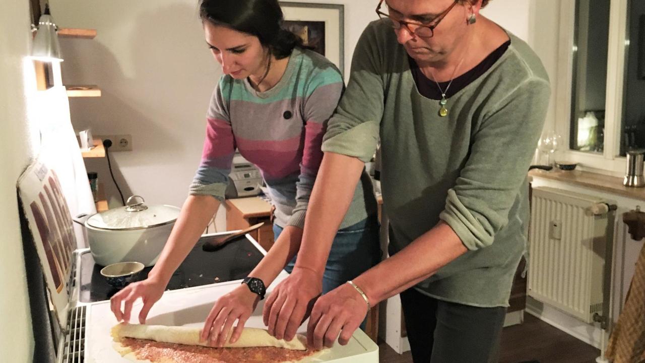Elna und ihre Tochter stehen zusammen in der Küche und rollen einen Teig ein. Elna und ihre Tochter stehen zusammen in der Küche und rollen einen Teig ein.
