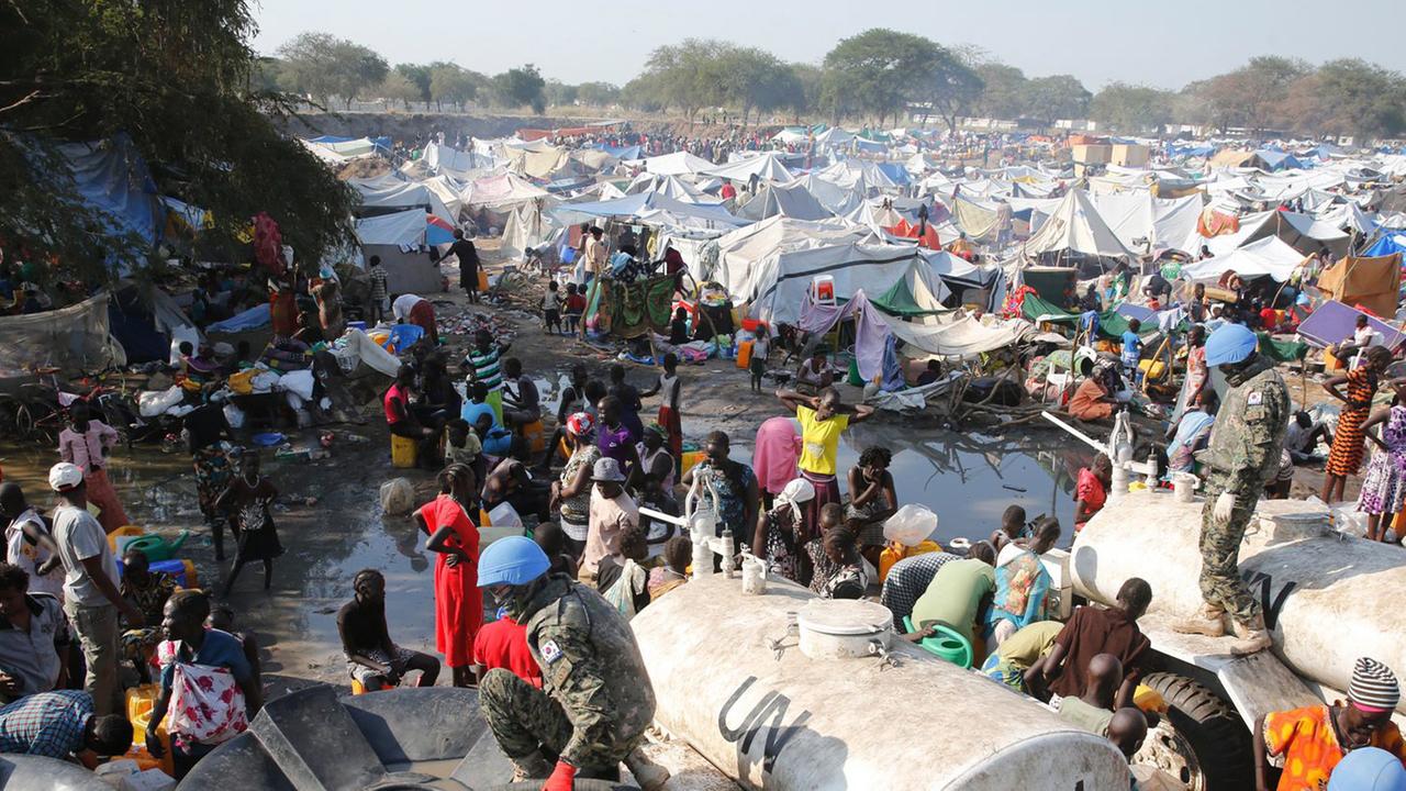In einem Flüchtlingscamp mit zahlreichen Zelten werden Wassertanks durch Soldaten befüllt.