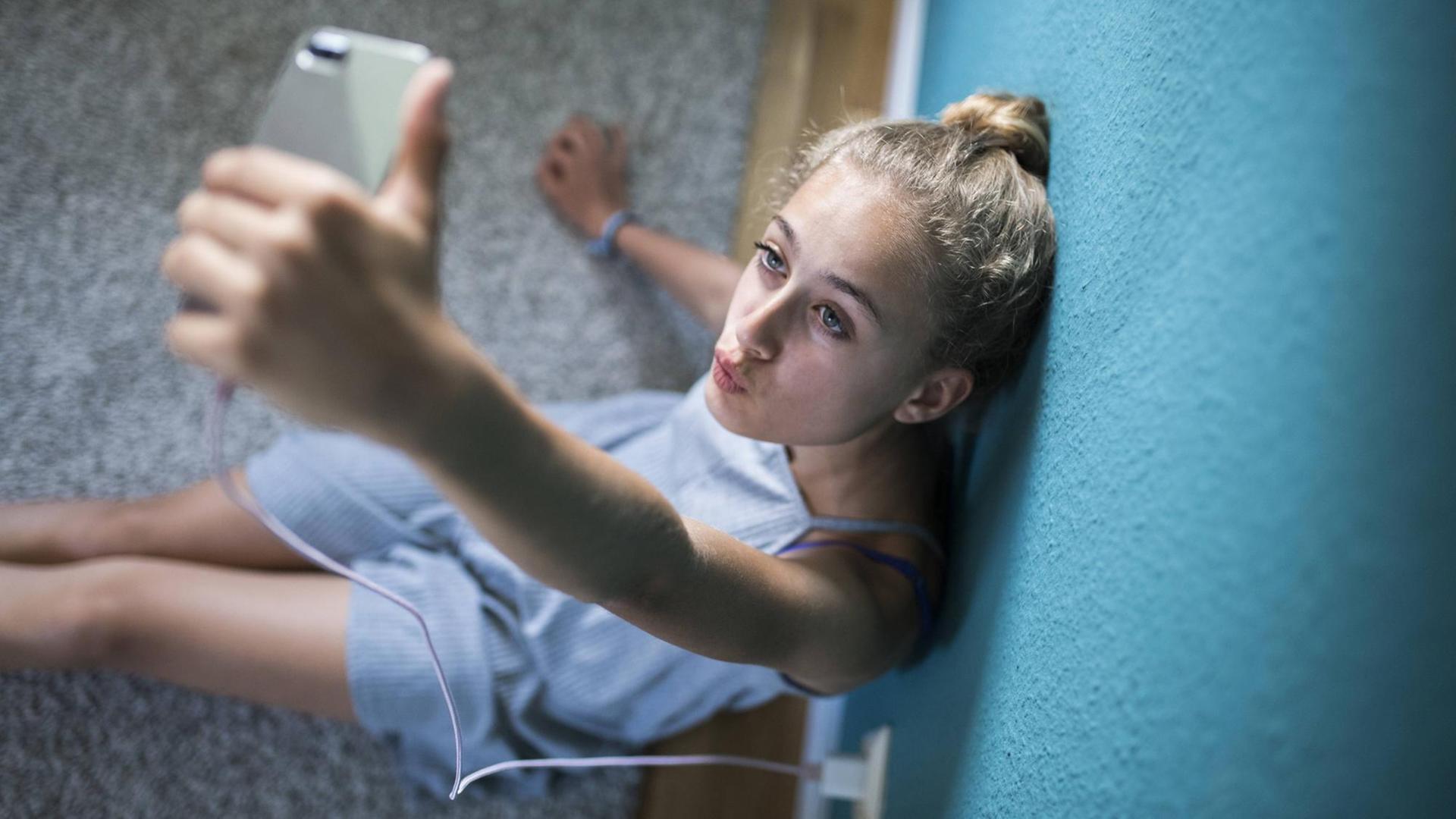Ein Mädchen sitzt in seinem Zimmer auf dem Boden und macht Selfies. Ein Mädchen sitzt in seinem Zimmer auf dem Boden und macht Selfies.