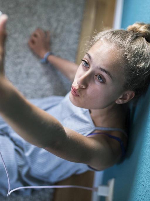 Ein Mädchen sitzt in seinem Zimmer auf dem Boden und macht Selfies.