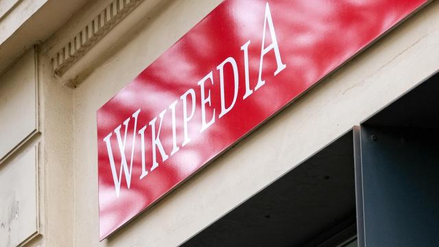 Ein rotes Schild mit der weißen Aufschrift "Wikipedia" über einem Ladenlokal.