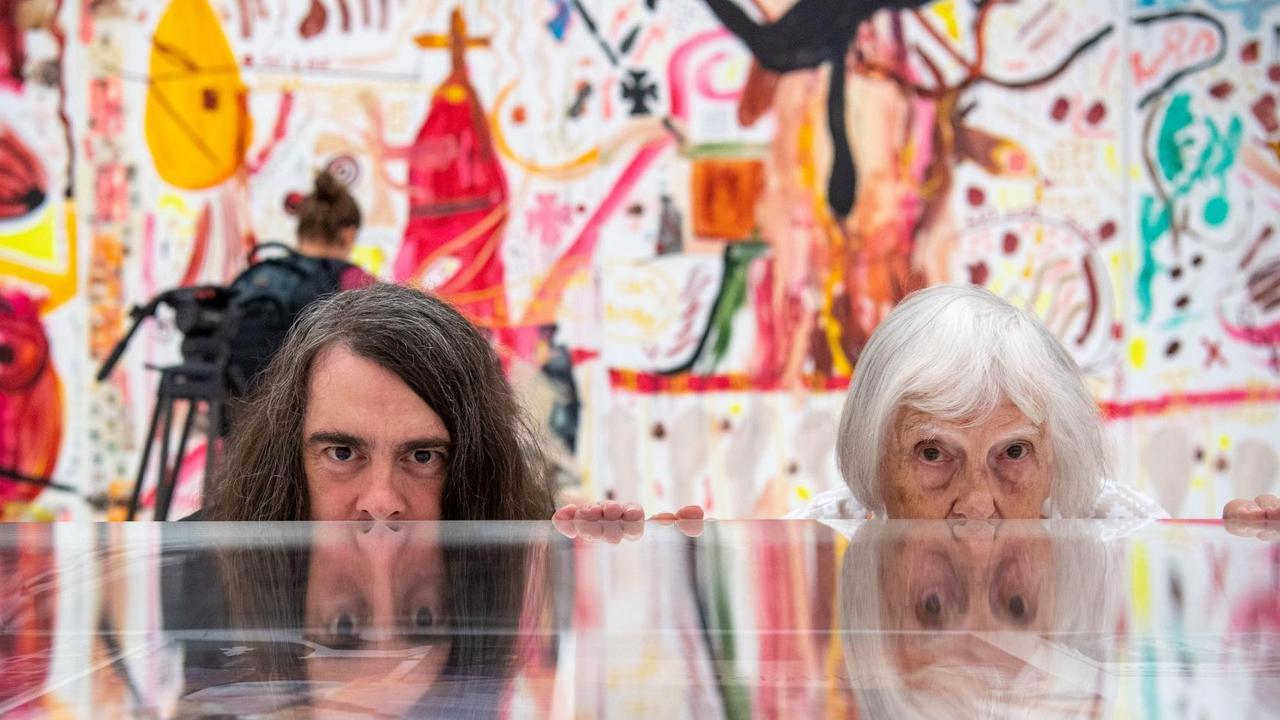 Brigitte und Jonathan Meese (Maler und Aktionskünstler) spiegeln sich im Ausstellungsraum in einem Schaukasten. Im Hintergrund sind Gemälde von Jonathan Meese zu sehen. Brigitte und Jonathan Meese (Maler und Aktionskünstler) spiegeln sich im Ausstellungsraum in einem Schaukasten. Im Hintergrund sind Gemälde von Jonathan Meese zu sehen.