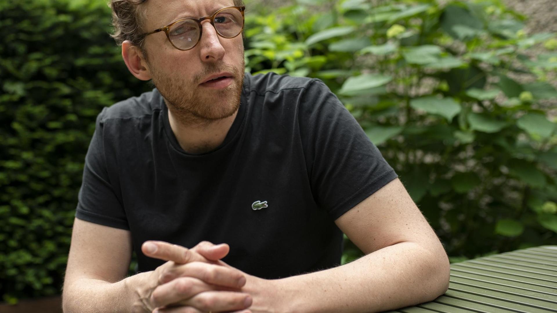 Johann König im Juni 2019 an einem Holztisch sitzend Johann König im Juni 2019 an einem Holztisch sitzend