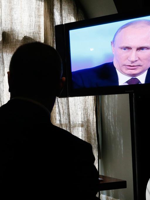 Ein Bildschirm zeigt die Fernsehsendung mit Wladimir Putin, davor als Schatten ein Zuschauer