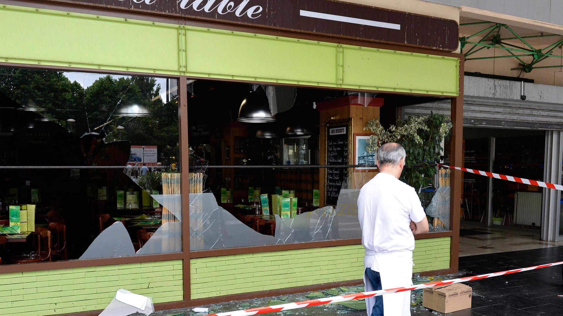 Ein Mann läuft hinter der Absperrung vor den Fenstern eines Restaurants im Pariser Bezirk Sarcelles, die bei Demonstrationen zerstört wurden. Ein Mann läuft hinter der Absperrung vor den Fenstern eines Restaurants im Pariser Bezirk Sarcelles, die bei Demonstrationen zerstört wurden.