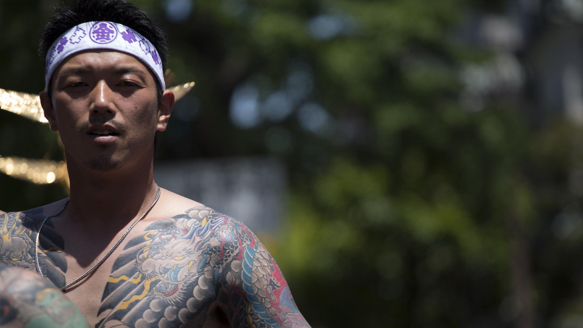 Ein junger Japaner zeigt seinen großflächig tätowierten Oberkörper. Er hat sich ein weißes Band mit lila Zeichen um den Kopf gebunden. Ein junger Japaner zeigt seinen großflächig tätowierten Oberkörper. Er hat sich ein weißes Band mit lila Zeichen um den Kopf gebunden.