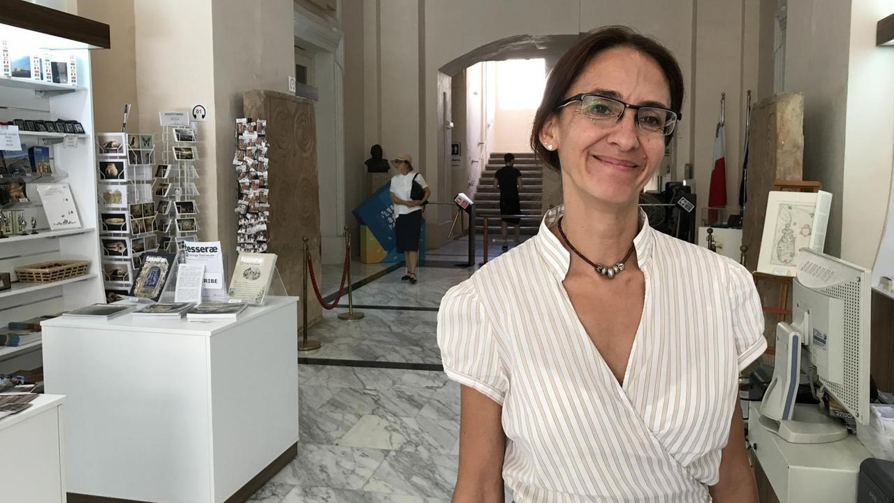 Sharon Sultana, Kuratorin des Nationalmuseums für Archäologie, steht im Eingangsbereich in weißem Hemd und strahlt.