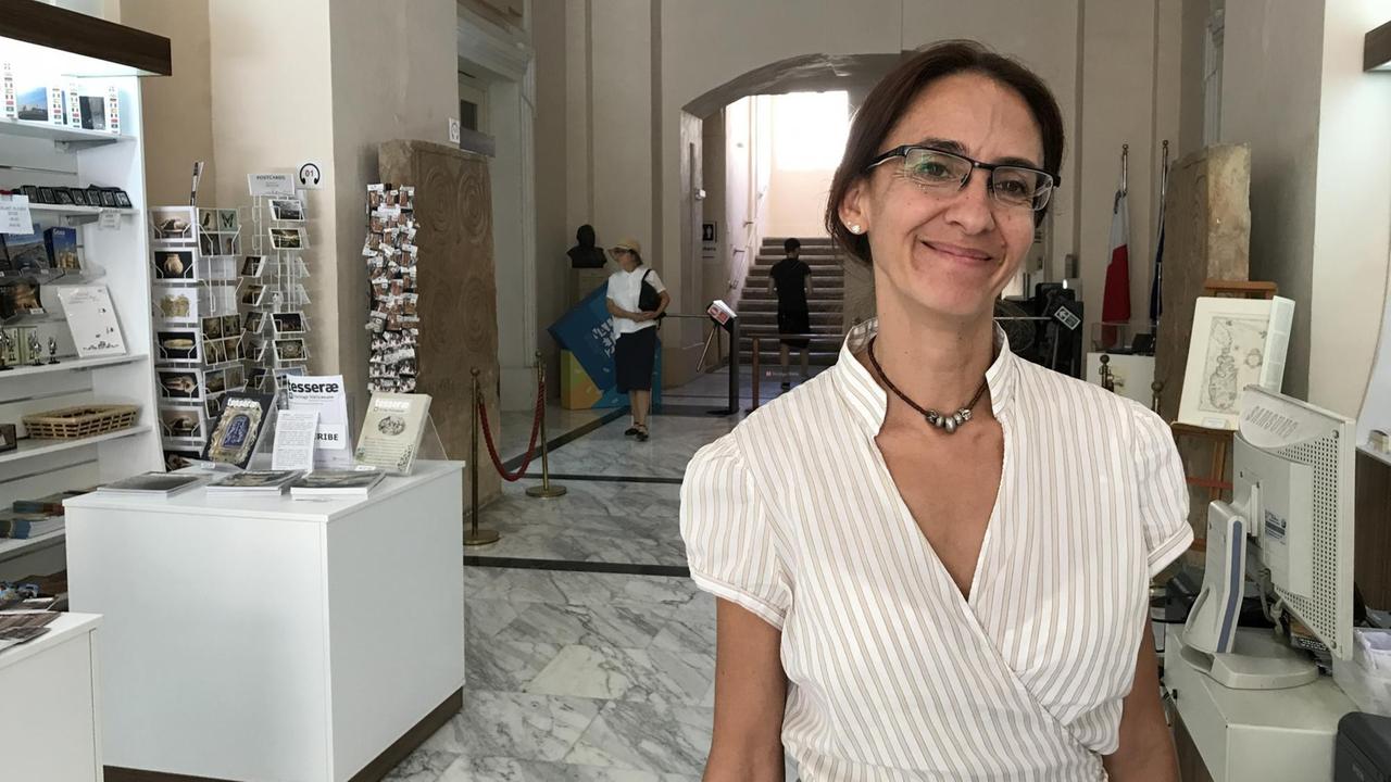 Sharon Sultana, Kuratorin des Nationalmuseums für Archäologie, steht im Eingangsbereich in weißem Hemd und strahlt. Sharon Sultana, Kuratorin des Nationalmuseums für Archäologie, steht im Eingangsbereich in weißem Hemd und strahlt.
