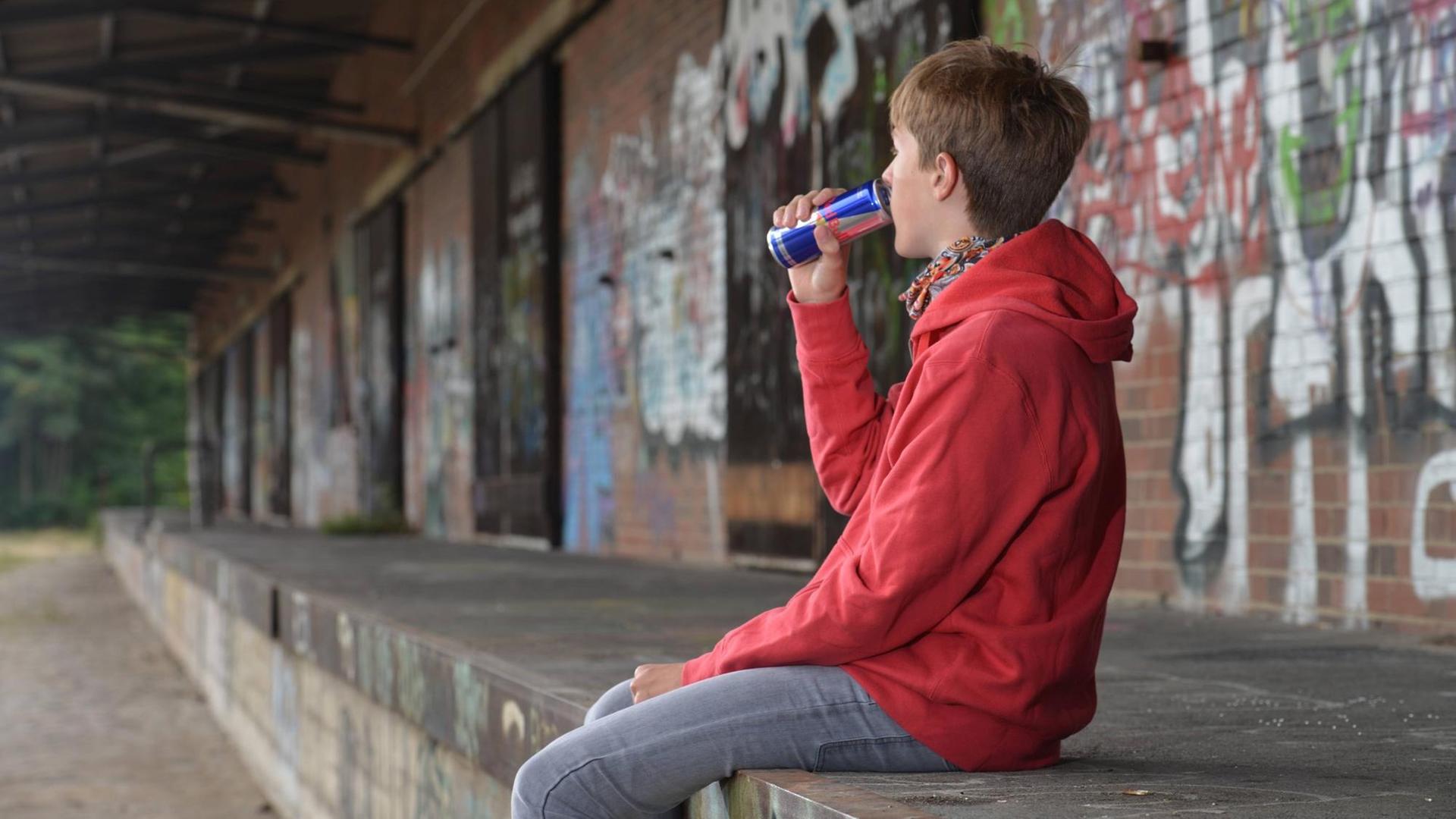 Ein Jugendlicher sitzt auf einer Steinmauer und trinkt einen Energy Drink. Ein Jugendlicher sitzt auf einer Steinmauer und trinkt einen Energy Drink.