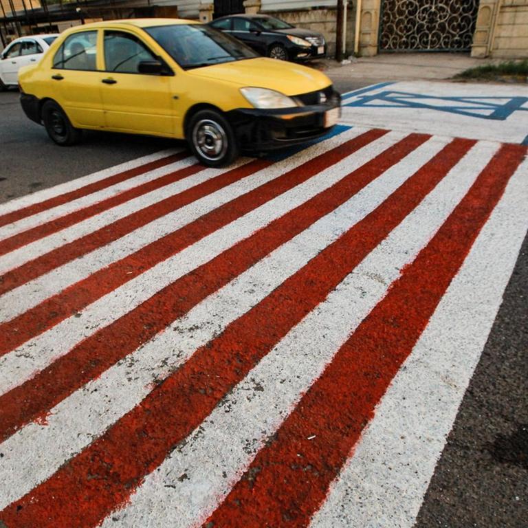 Ein Auto fährt über eine Flagge der USA und einer Flagge von Israel, die auf die Straße gemalt wurden. 